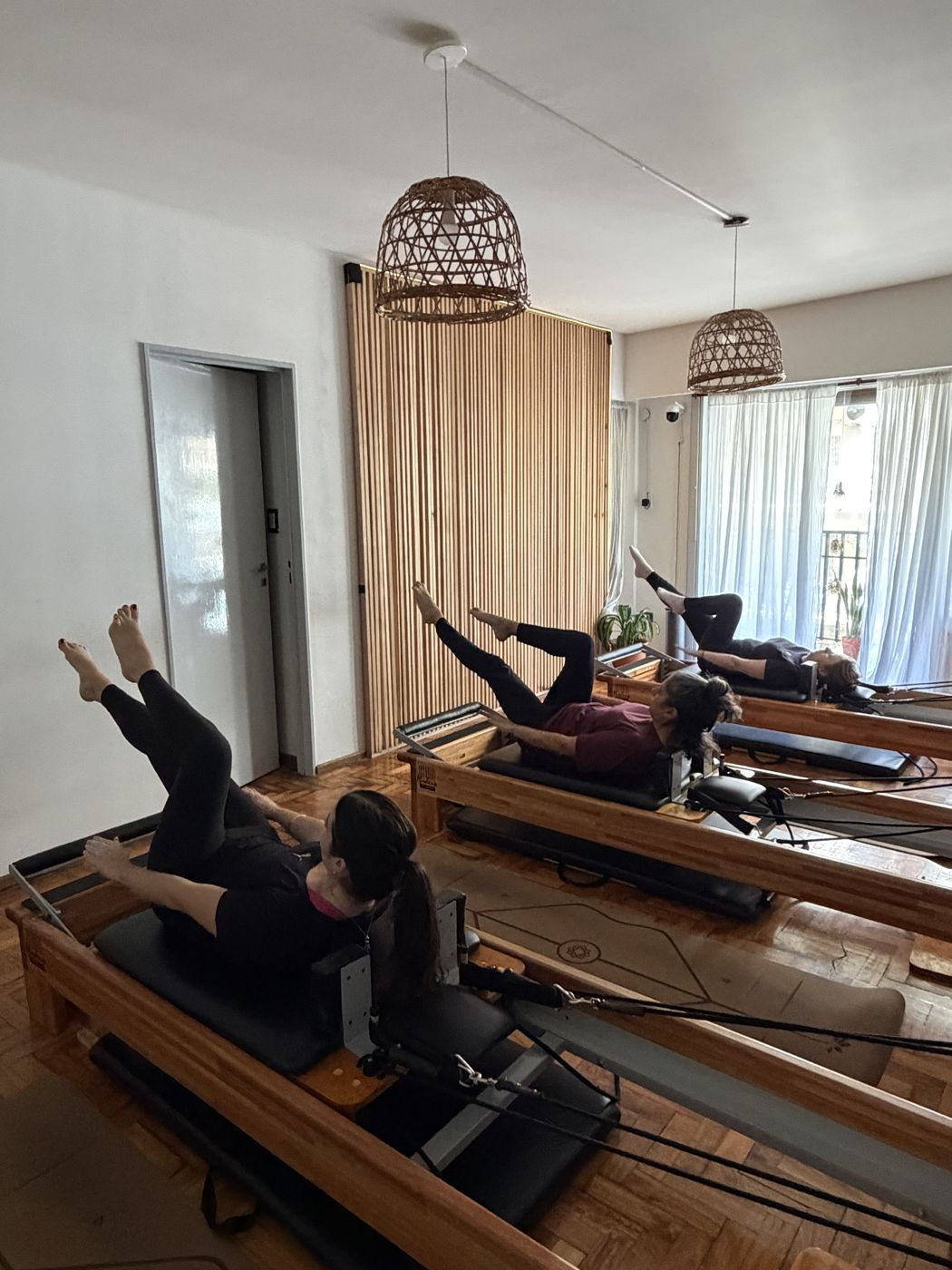 Tres alumnas en reformers elevando las piernas durante una clase grupal